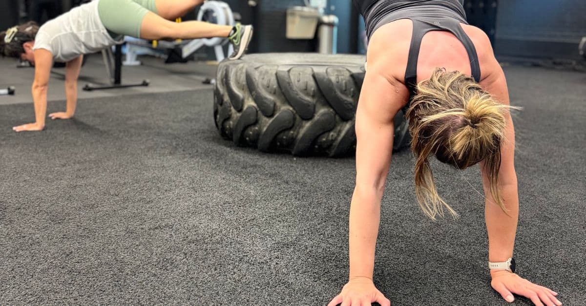 2 ladies during a fitness class with hands on floor and feet on tire